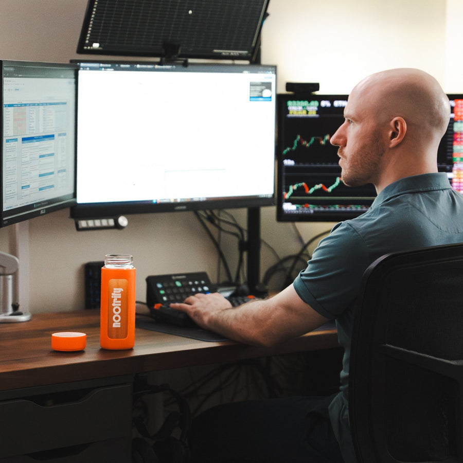 Nootrify bottle on a desk beside someone working at three monitors
